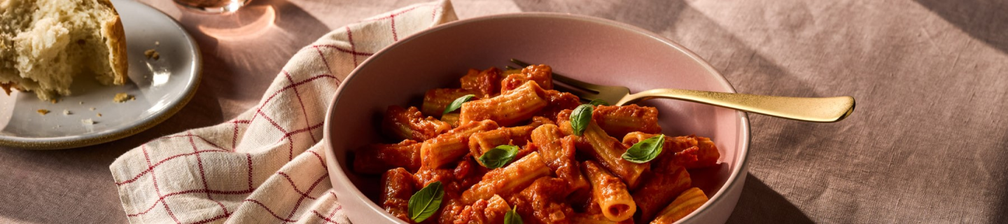 Bowl of rigatoni pasta with Rao's® tomato sauce and fresh basil on a rustic table setting